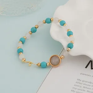 Close-up detail of turquoise and white bead bracelet with elegant gold tone metal charms.