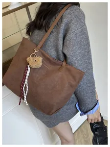 Detailed view of brown tote bag with cute bear charm and shoulder strap for daily commuting.