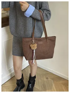 Brown suede tote bag detail showing plush bear pendant and double shoulder straps.