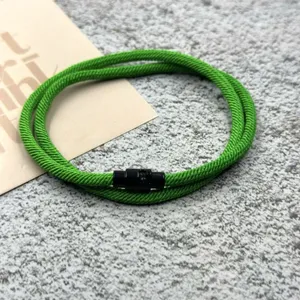 Detail of the green braided rope bracelet featuring a sleek black magnetic clasp on texture.