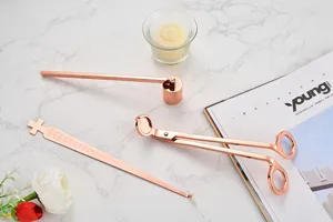 Close-up of rose gold candle tool set details on marble background, elegant wick trimmer.