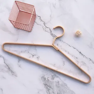 Close up view of luxury gold aluminum clothes hanger on white marble surface with wire basket.