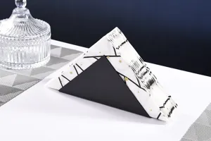 Closeup detail showing the modern black metal triangular napkin holder on white table.