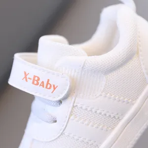 Dettaglio in primo piano di sneaker bianca per neonati, tomaia in rete traspirante, velcro.