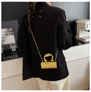 Mini gold metallic cylindrical shoulder bag with abstract handle and chain strap for women.