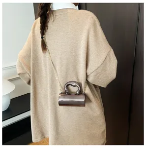 Detail view of stylish glossy PVC cylinder mini crossbody handbag in metallic finish worn on sweater.