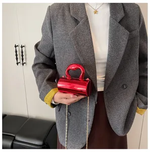 Detailed view of the shiny red cylindrical handbag with metal handle and chain strap.