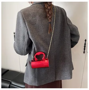 Glossy red PVC cylinder shoulder bag detail, stylish mini crossbody design with gold chain strap.