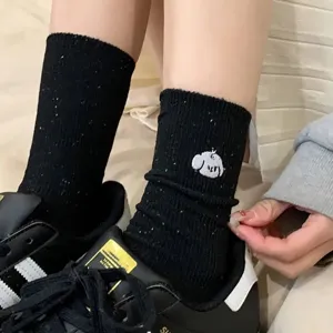 Detail view of women black mid-calf socks with cute cartoon embroidery and colorful flecks.