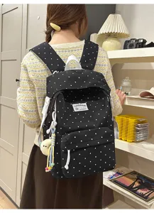 Detailansicht eines süßen schwarzen Pünktchen-Rucksacks mit weißen Trägern und Anhänger.