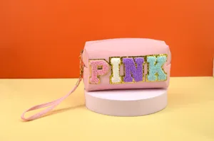 Pink cosmetic bag detail showing embroidered letter design, soft wrist strap and zipper.