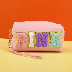 Detail shot of pink cosmetic storage bag with colorful embroidered letters and wristlet zipper.