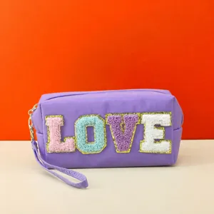 Detailed view of the purple cosmetic bag featuring colorful chenille LOVE letters and wrist strap.