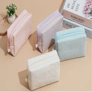 Detailed shot of pastel tweed cosmetic bags featuring pearl zipper pulls and spacious storage.