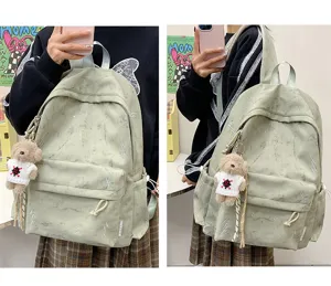 Detailed view of green backpack with white lightning print and teddy bear keychain.