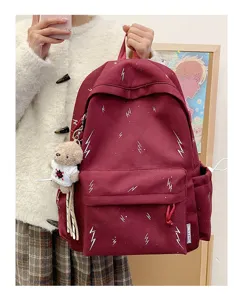 Detailed view of burgundy student backpack featuring lightning print and teddy bear charm