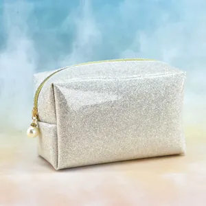Close-up of shimmering silver cosmetic makeup bag with gold zipper and pearl pendant detail.