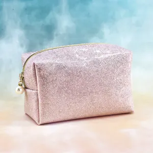 Pink glitter cosmetic bag with gold zipper and pearl charm detail, cute portable makeup storage.