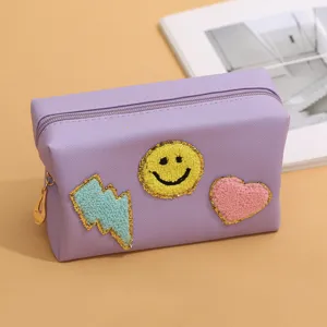 Close-up detail of a purple cosmetic storage bag with cute plush smiley face and heart patches.