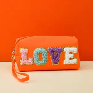Close-up view of orange cosmetic pouch with colorful textured LOVE letters and wrist strap.