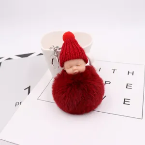 Süßer schlafender Baby Puppen Schlüsselanhänger mit rotem flauschigen Bommel und Mütze.