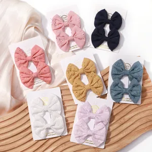 Set of seven colorful embroidered fabric bow hair clips for kids on white display cards.
