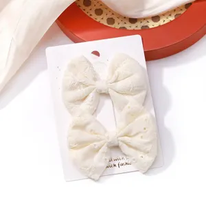 Close-up of two off-white embroidered fabric bow hair clips for kids on a card.