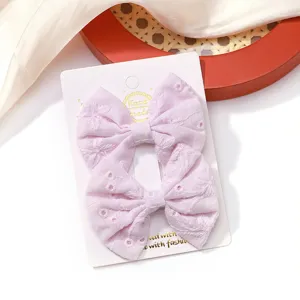 Macro view of light purple fabric bow hair clips featuring delicate floral embroidery patterns