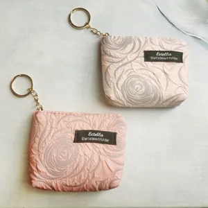 Close-up detail of mini pink coin purse with rose texture, zipper and gold keychain.