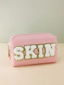 Close-up of pink PU leather cosmetic bag with white chenille letter patch SKIN and gold zipper.