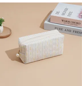 Tweed cosmetic bag detail with soft woven fabric, zipper closure, and pearl pull for travel use.