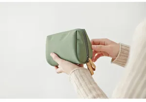 Nahaufnahme einer tragbaren mini grünen Kosmetiktasche mit Reißverschluss und Lederlaschen.