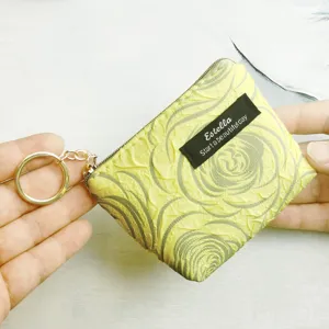 Detail view of mini yellow coin purse with key ring and fabric tag, compact daily accessory.