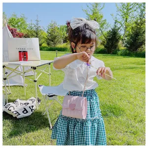 Little girl modeling a pink quilted mini crossbody bag with heart detail in a sunny garden