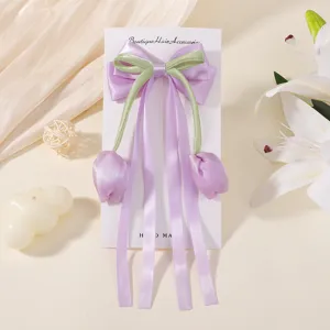 Detalle de una pinza para el pelo con lazo de tulipán morado y cintas largas en tarjeta.