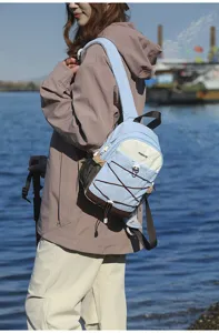 Detail view of a small blue and beige outdoor backpack worn by a model in nature.