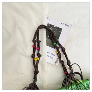 Detail of green woven tote bag with braided brown straps and colorful beads