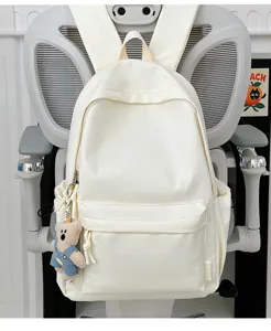 Detailopname van een witte minimalistische schooltas met een schattige pluche beer sleutelhanger.