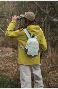 Young woman wearing a small light green color-block hiking backpack in a forest setting