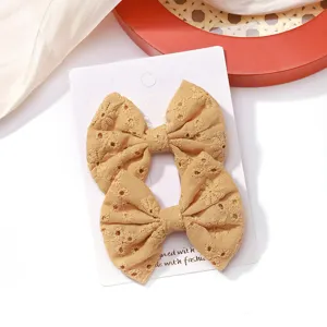 Detailed view of two yellow embroidered fabric bow hair clips with floral patterns on card.