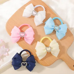 Close-up detail of cute kids hair ties with ribbon bows and sparkling rhinestone hearts.