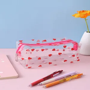 Detailed view of a transparent pencil case with red heart prints, set on a pink desk.