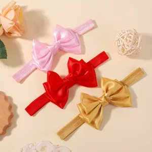 Vue détaillée de trois bandeaux pour bébé avec nœuds en satin élégants en rose, rouge et doré