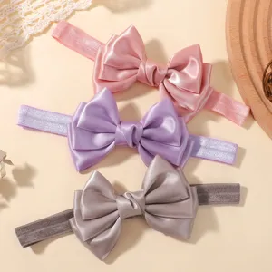 Gros plan de trois bandeaux bébé avec nœuds en satin rose, lavande et gris argenté