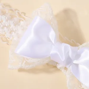 Detailopname van een witte satijnen strik en kanten rand op een elastische babyhoofdband