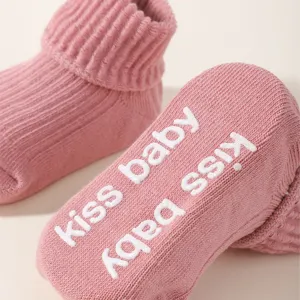 Detailed view of pink knitted baby socks with anti-slip 'kiss baby' lettering on the sole