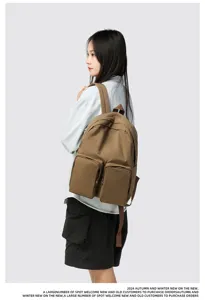 Detail view of a large capacity brown casual backpack with double front pockets worn by a model
