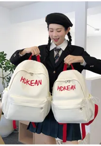 Mannequin étudiante asiatique posant avec deux sacs à dos blancs brodés en salle