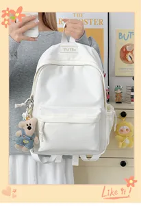 Vue détaillée d'un sac à dos scolaire blanc minimaliste avec un pendentif ours.