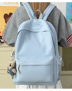 Gros plan d'un sac à dos d'écolier bleu clair muni d'un porte-clés ourson en peluche mignon.